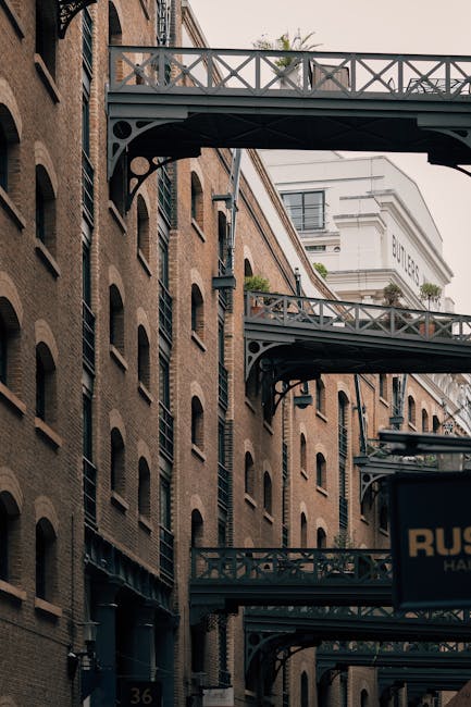 The image depicts a section of a historic brick building with multiple levels, featuring black cast iron fire escape balconies extending from the facade, connected by a network of stairs and walkways.